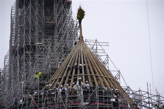 De timmerlieden laten een boeket bloemen achter boven op het geraamte van het dak tijdens de restauratie van de Notre-Dame in Parijs (AP Photo/Christophe Ena/La Presse)