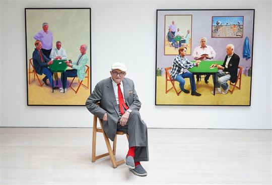 David Hockney zit voor enkele van zijn schilderijen die in Londen te zien zijn als onderdeel van de tentoonstelling ‘Painting and Photography’ uit 2015 (© Ansa/Epa/Andy Rain)