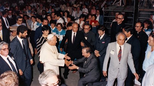 Don Giussani knielt bij de aankomst van Johannes Paulus II op de Meeting in de zomer van 1982. Links van de paus staat Emilia Guarnieri (© Meeting Rimini)